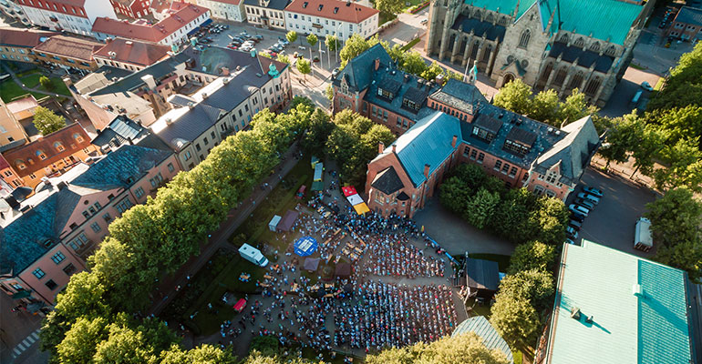 Flygfoto över Skara och folkvimlet på Djäkneplatsen under en sommarkväll. 