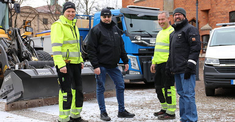 Fyra män står utomhus vid tre fordon.