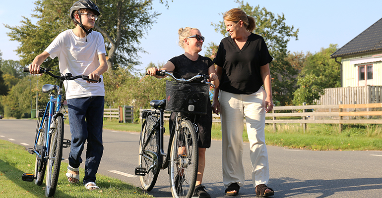 Två cyklister leder sina cyklar och samtalar med en kvinna.