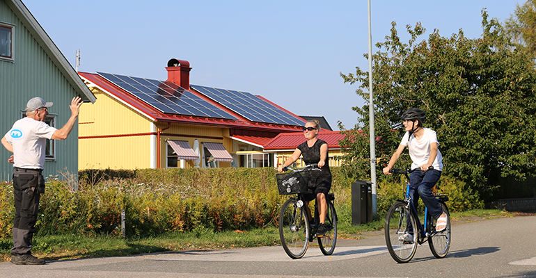 En äldre man hejar på två cyklister på en gata.