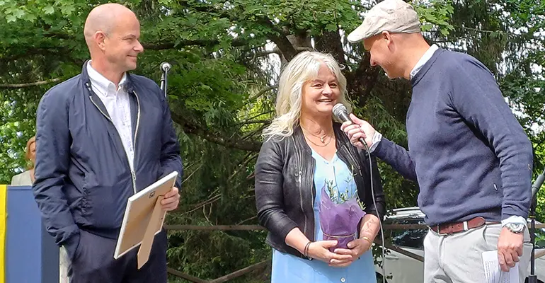 Två personer mottar diplom och blommor och blir intervjuade på scen.