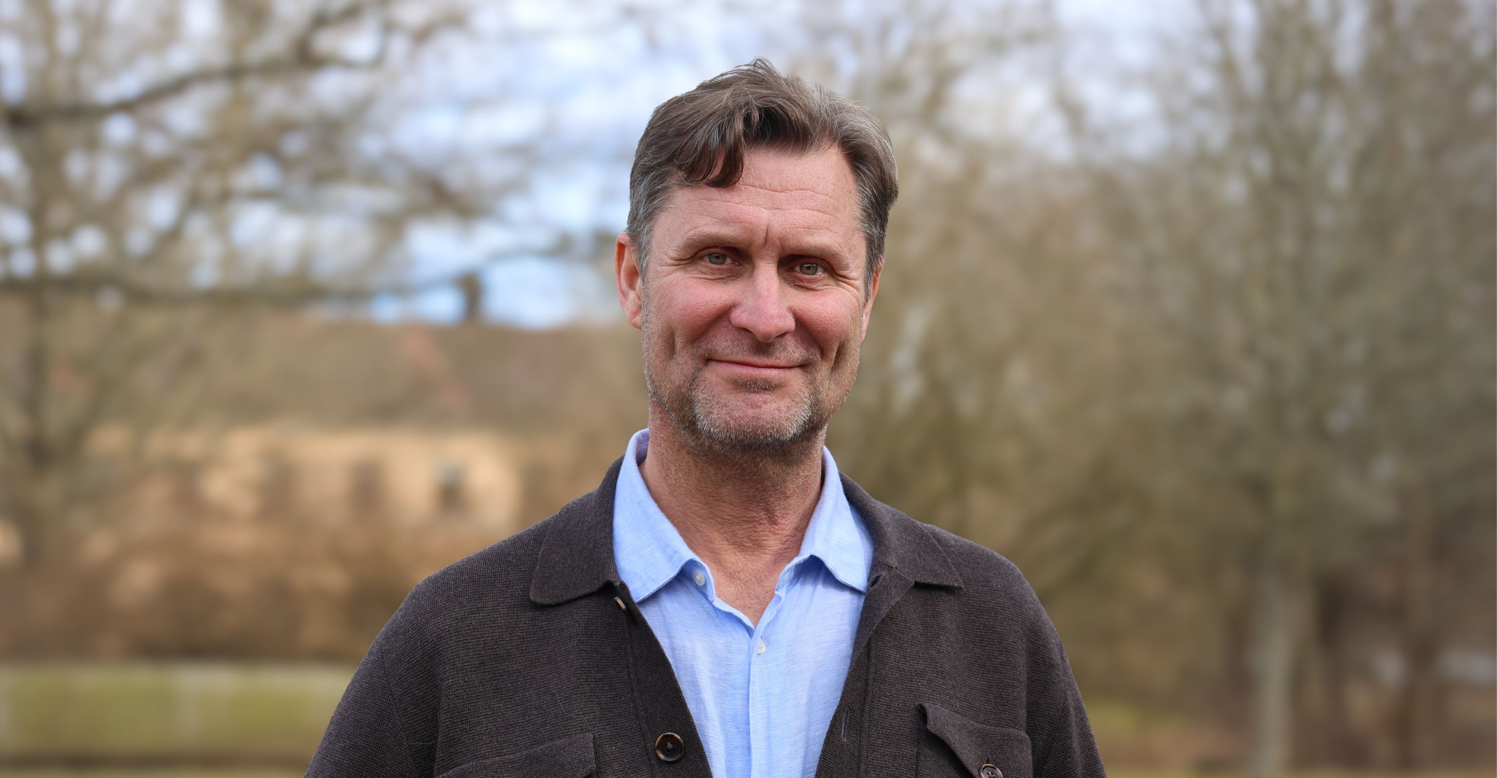 Porträtt av en leende man utomhus under en molnig dag.