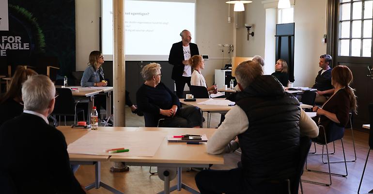En man står inför en hel grupp människor och presenterar en workshop.