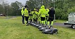 Nio robotgräsklippare på en gräsmatta. Ett tiotal personer med gula reflexkläder står runt omkring. 